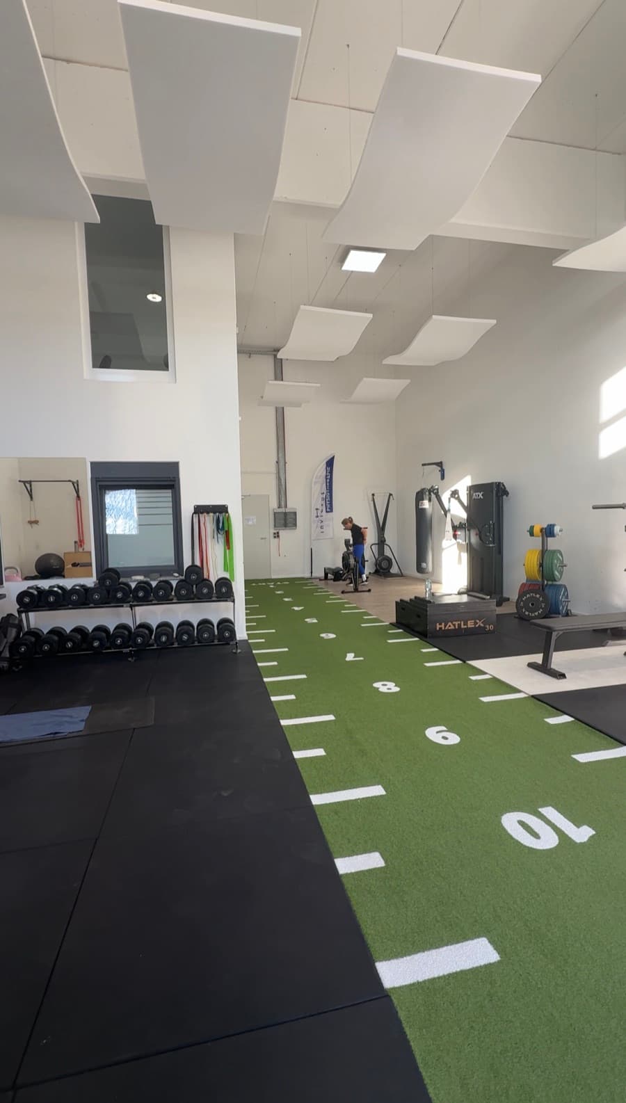 Trainingshalle 1 heute: grüne Sprintbahn mit Metermarkierung, Hantelablage, Rack und Schlagsack, geschwungene Akustiksegel unter der hohen Decke.