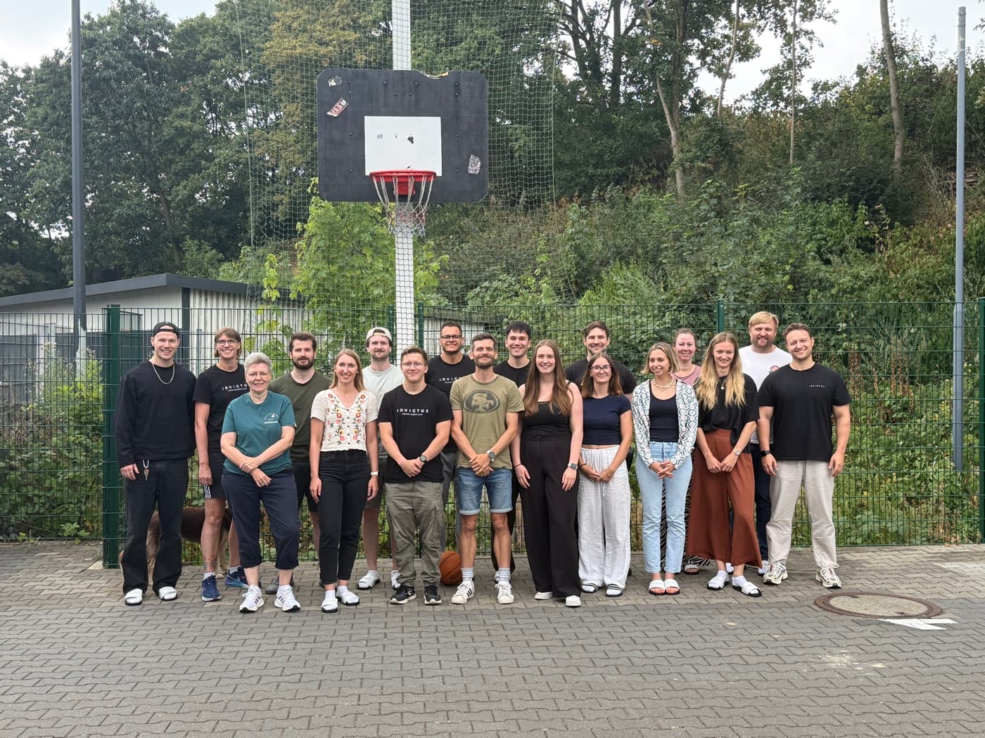 Das Invictus-Team, rund zwanzig Personen, aufgestellt vor einem Basketballkorb auf dem Außengelände in Leverkusen.